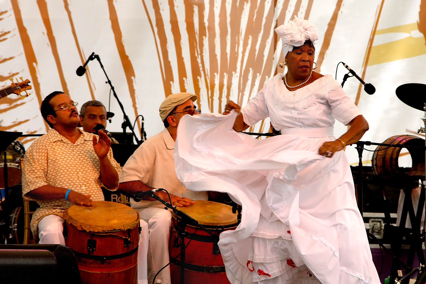 La Bomba Dancer in a white dress and a white bow dancing in front of drummers