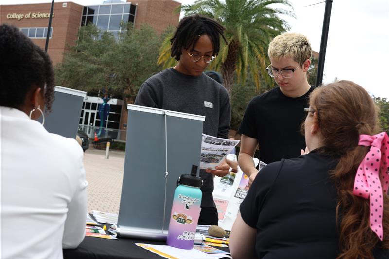 Students reviewing Study abroad materials at a UCF Abroad tabling event with two ladies at the table helping them